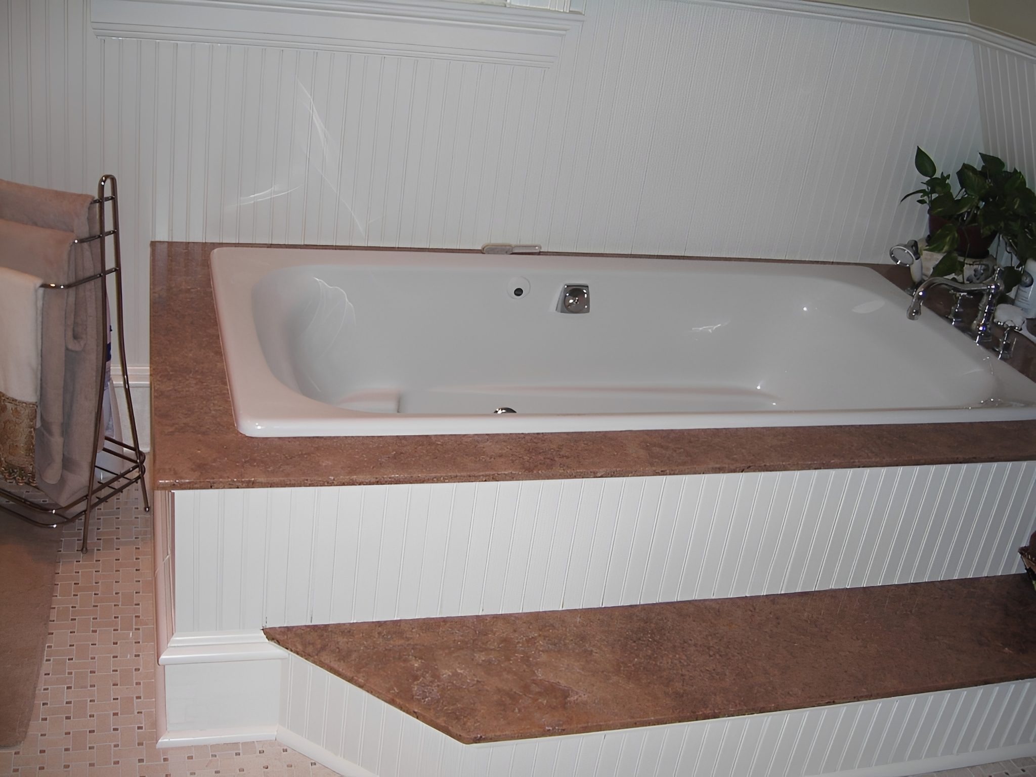 Bathtub with brown countertop and white paneling.